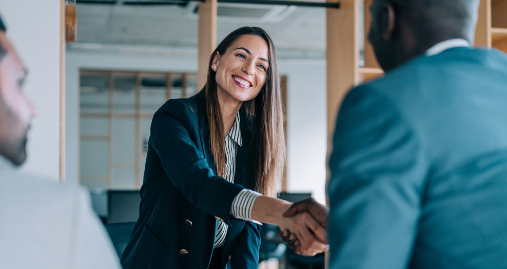 Insurance professional smiles and shakes hands with a client during a meeting.