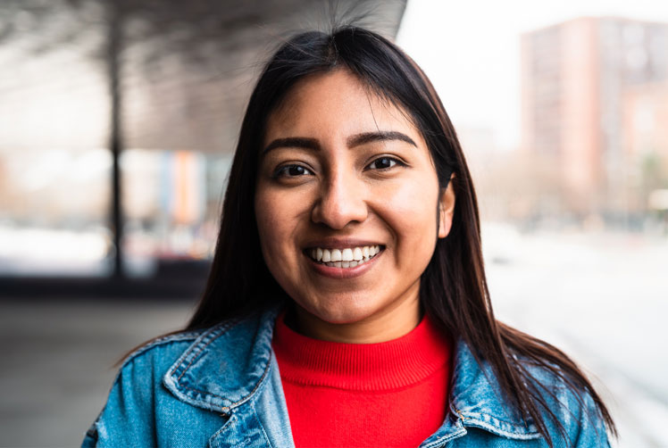 Student wearing a jean jacket smiles in an outdoor setting.