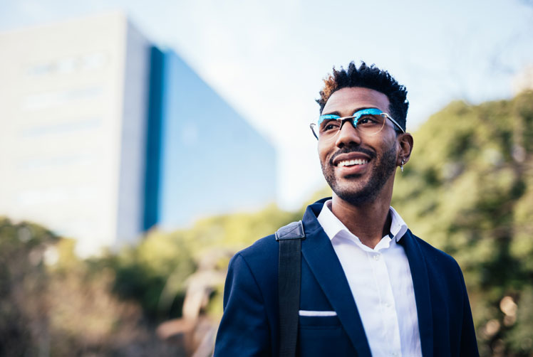 Insurance professional in glasses and a blazer smiles outdoors near an office building.