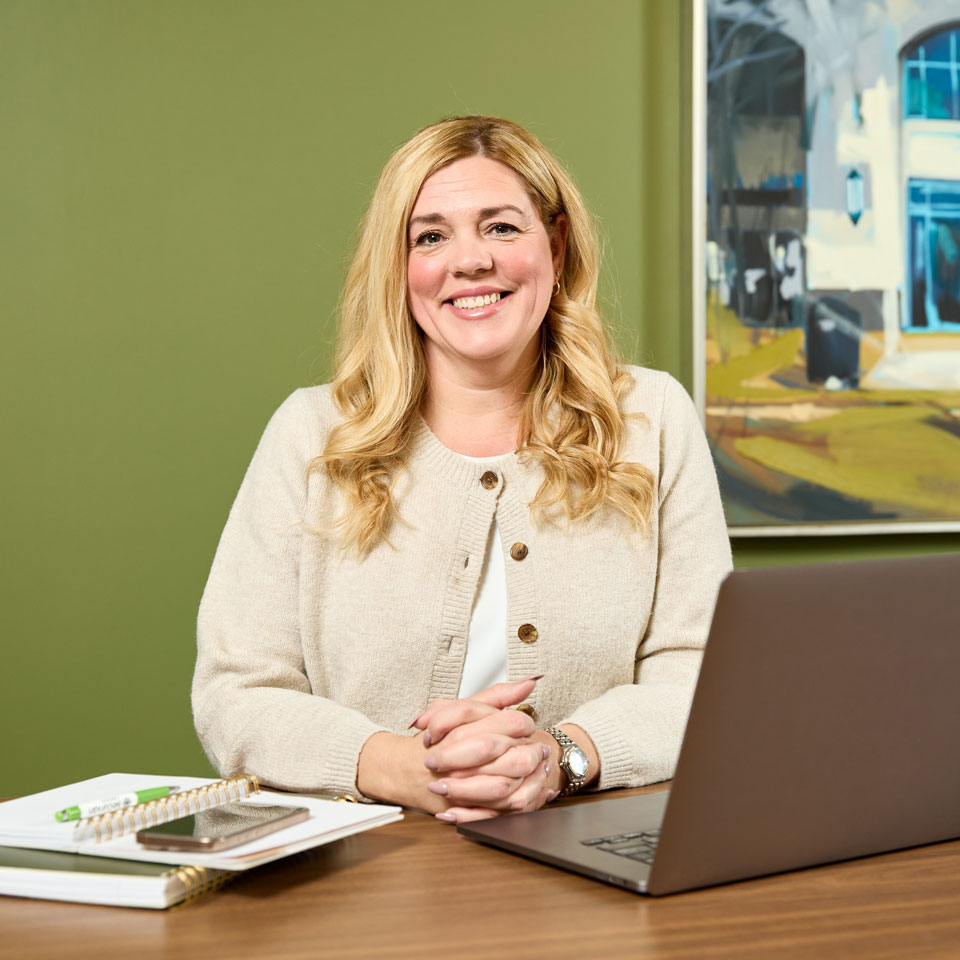 Securian Canada employee smiles while seated at a desk with an open laptop.