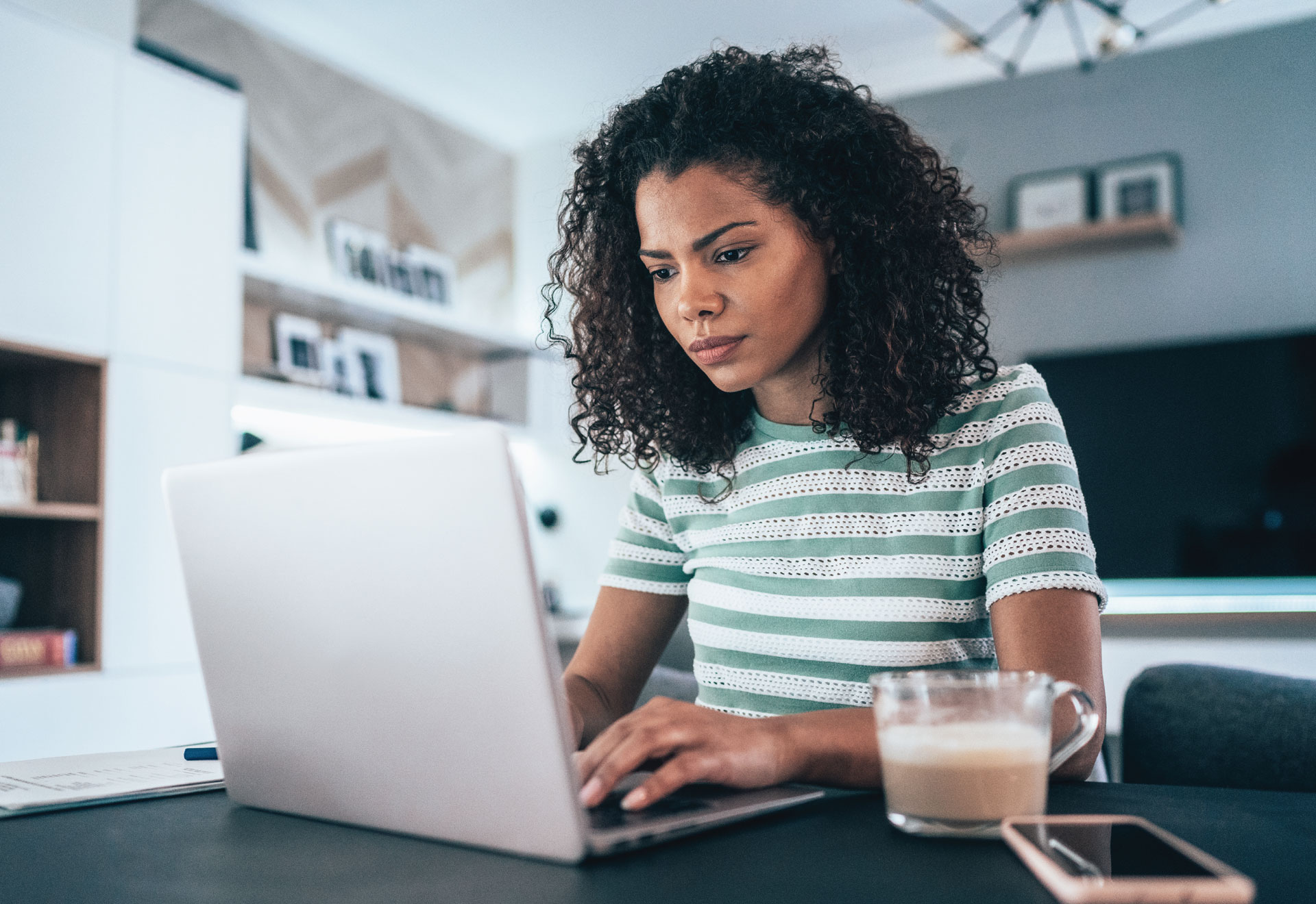 Person with long hair works on a laptop in a home office surrounded by a graphic green halo.