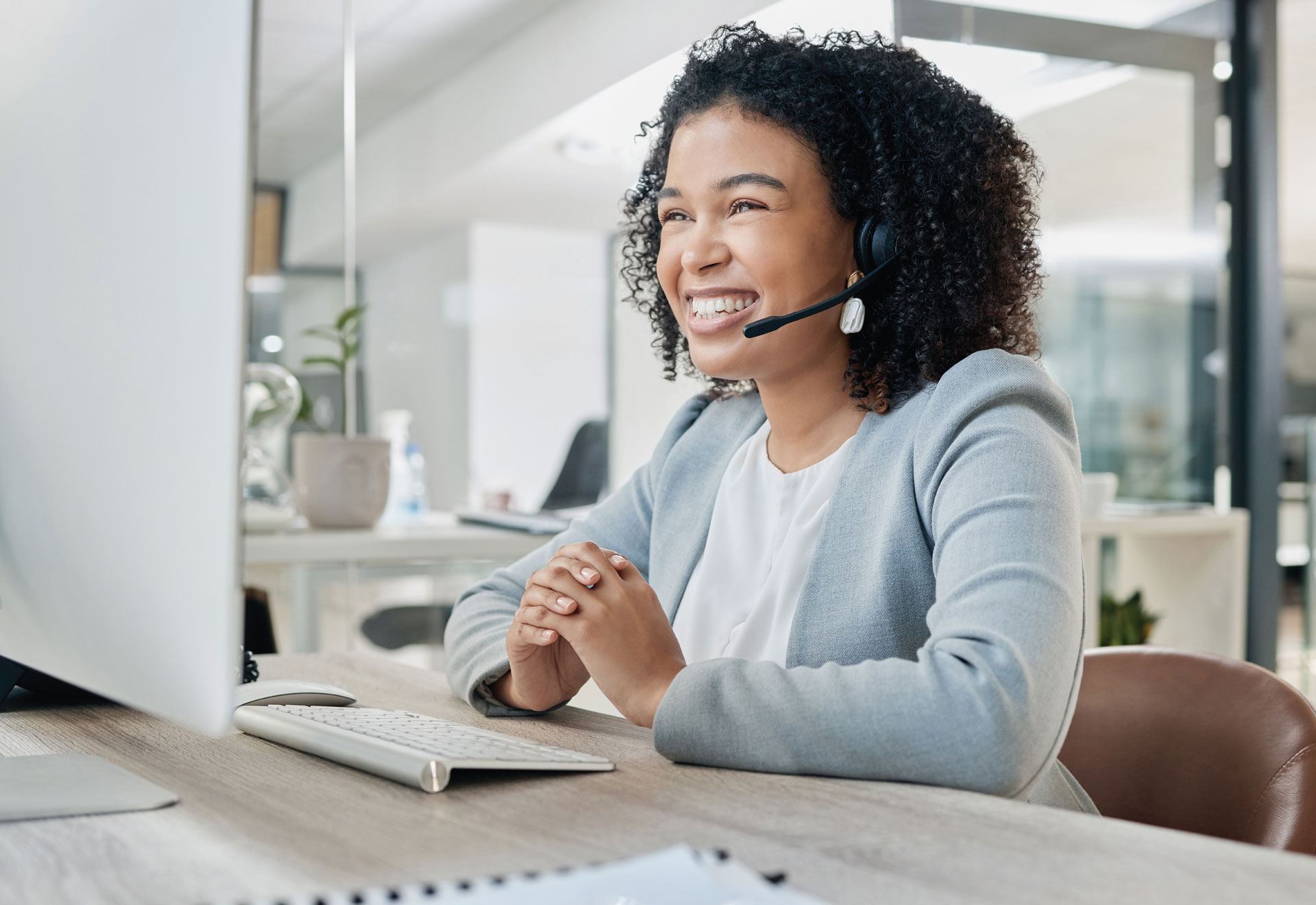 Professional person wearing a headset smiles while sitting in front of a desktop computer.