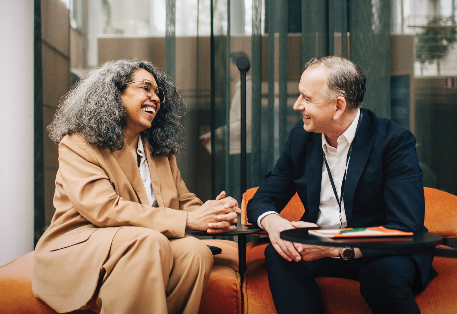Two executives sit and chat in an office setting.