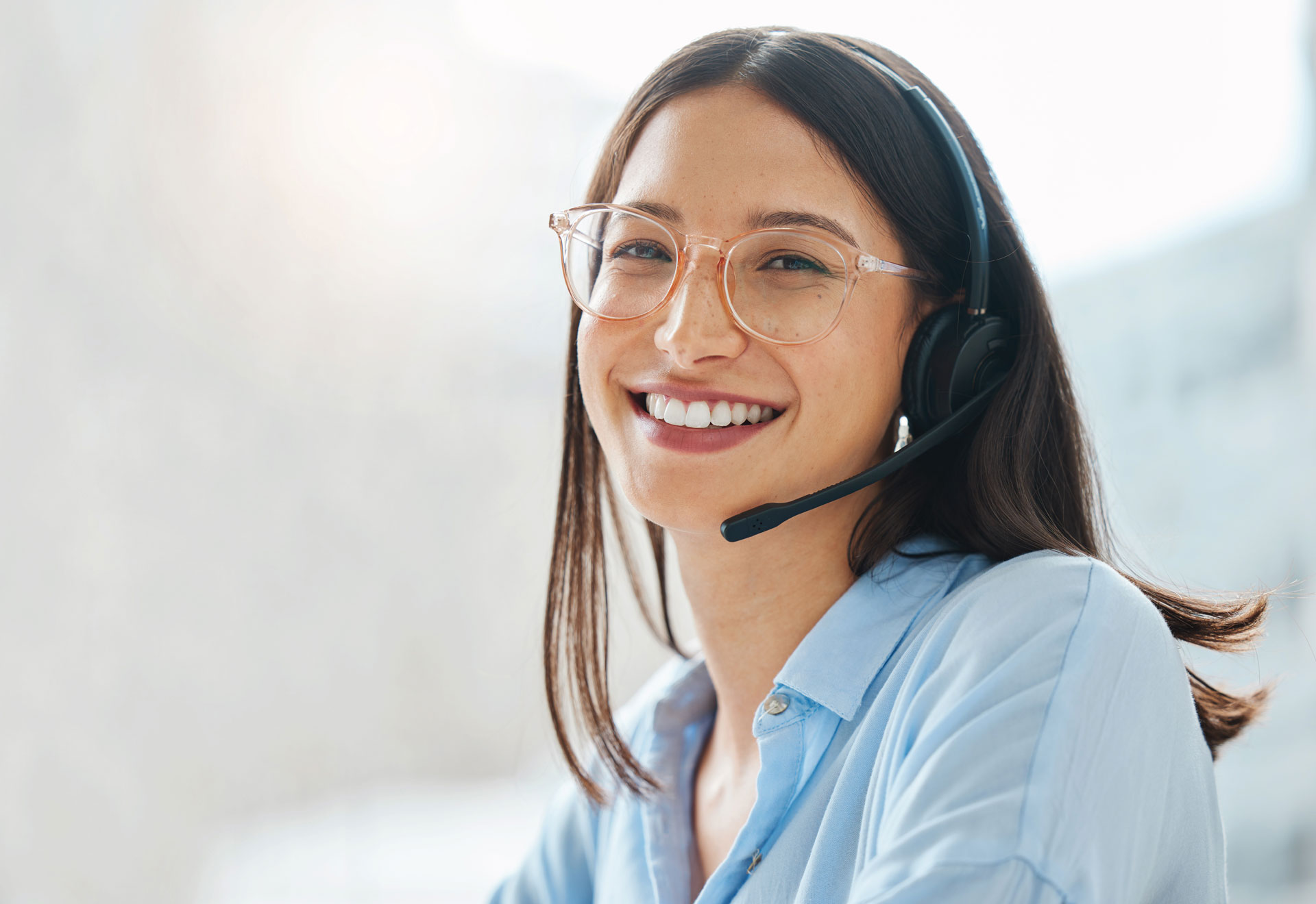 Professional person wearing glasses and a headset smiles.