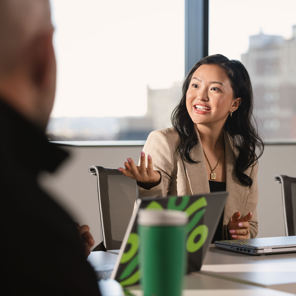Business professional gestures across a conference table while speaking with a colleague.