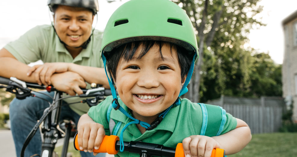 An adult and child wearing green bike helmets smile while stopped on their bicycles.