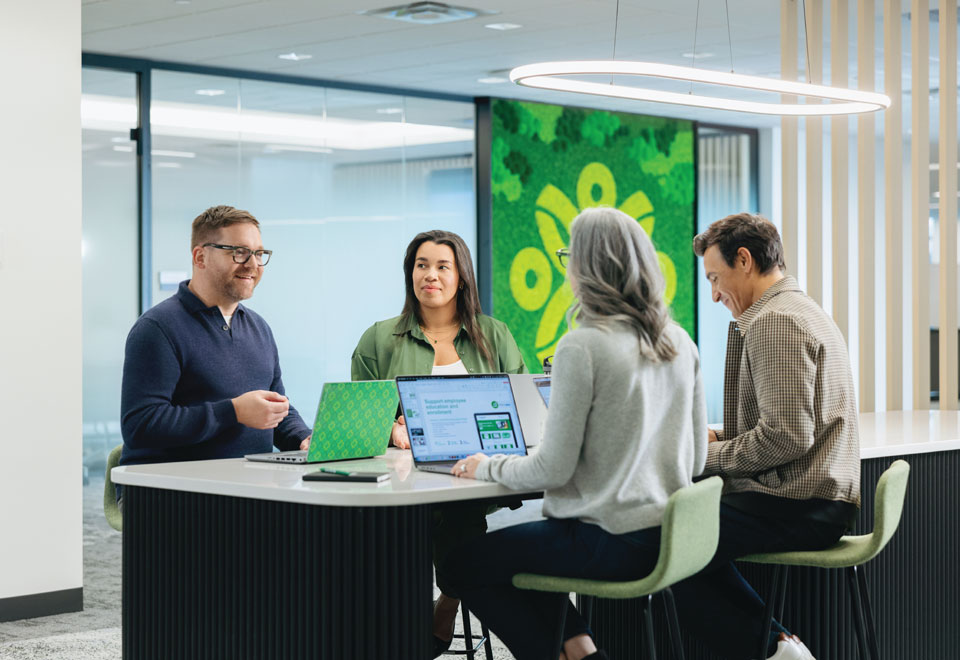 Group of Securian Canada employees chat during a meeting with laptops open in front of them.