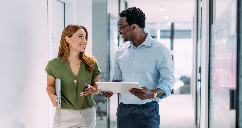 Two Securian Canada colleagues chat while walking through an office hallway.