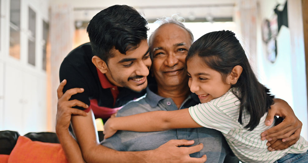An elderly person smiles while being embraced by younger family members.