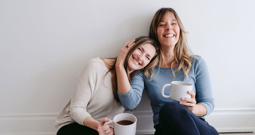 Two friends smile and embrace while having a coffee.