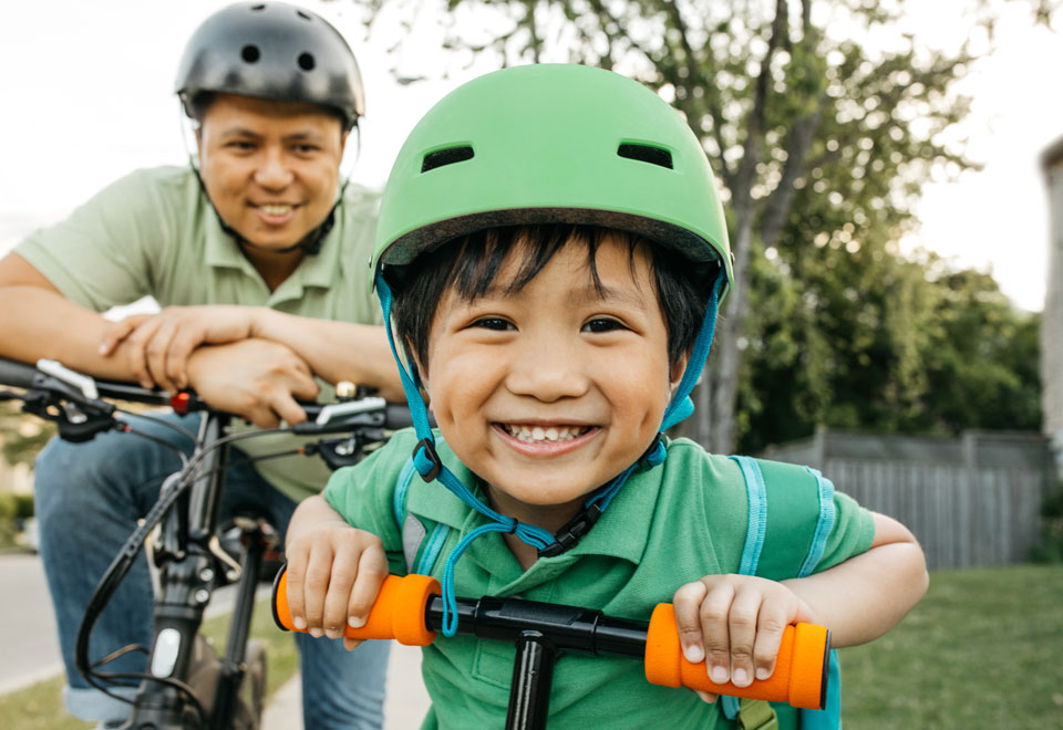 An adult and child wearing green bike helmets smile while stopped on their bicycles.