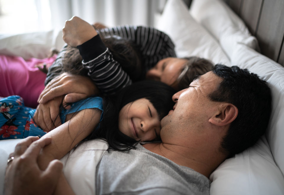 Young family lies on a bed together smiling.