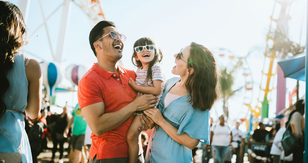 Young family wearing sunglasses smile together and laugh at a carnival.