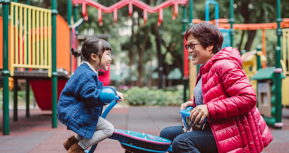 Grandparent and grandchild play in a playground together.