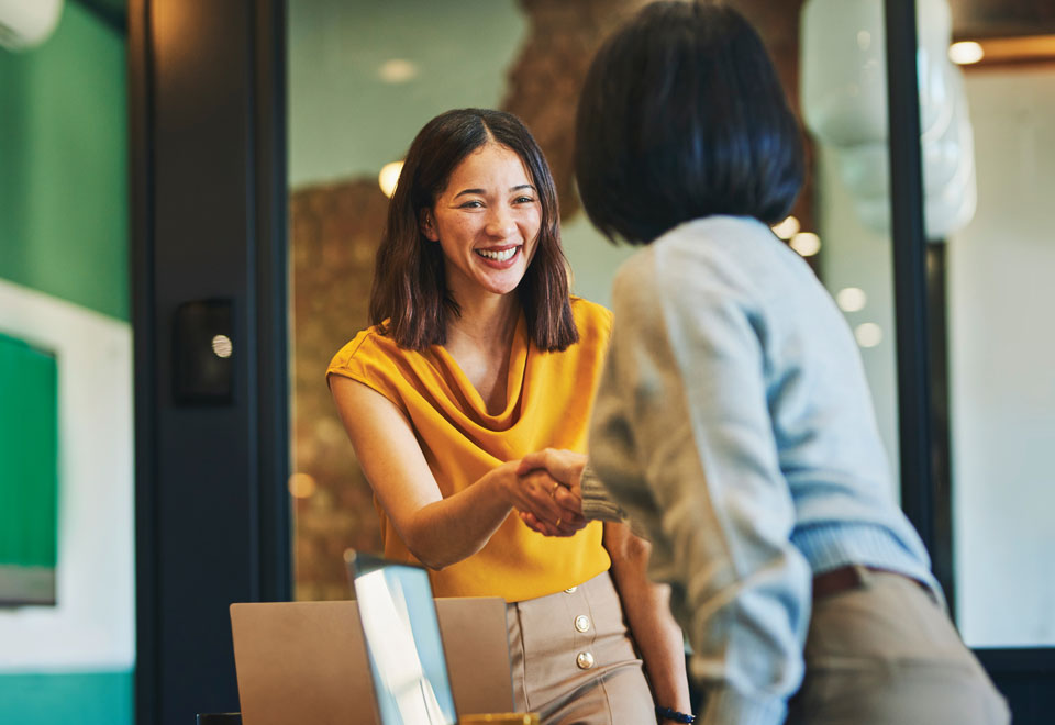 Two people smile while shaking hands in a boardroom.
