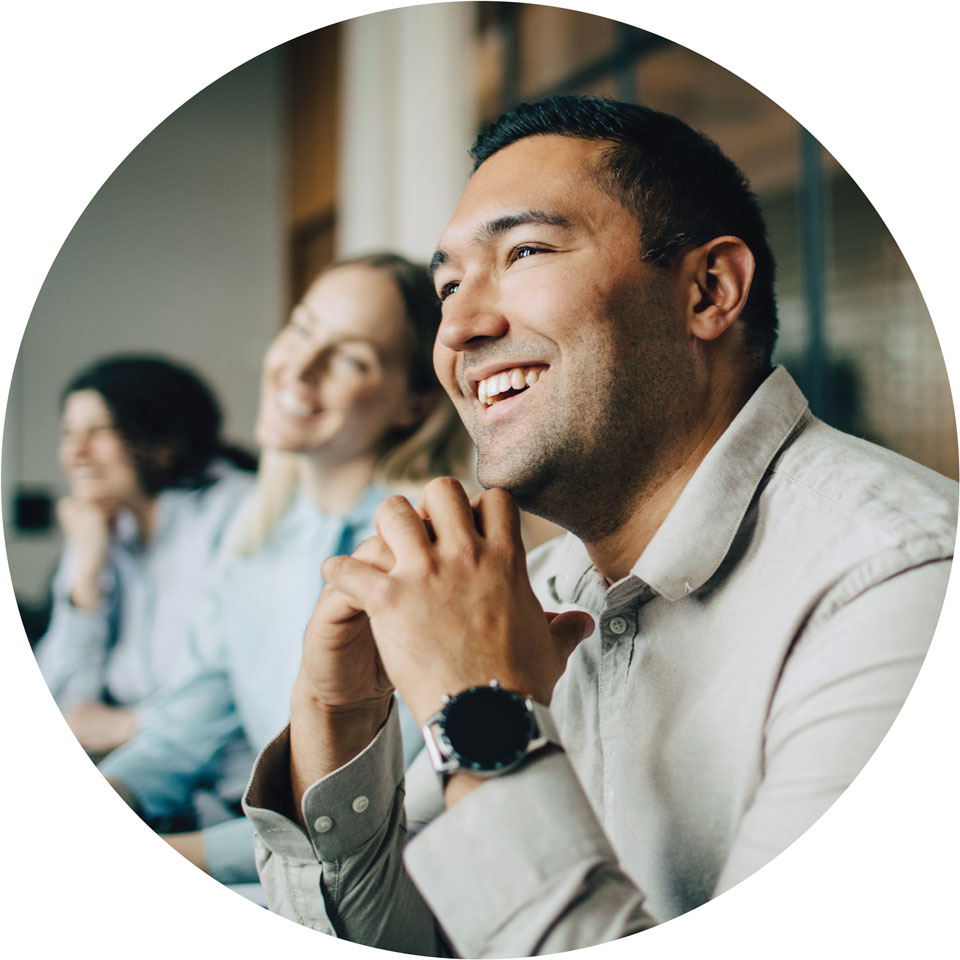 Colleagues sit and smile during a presentation in an office.