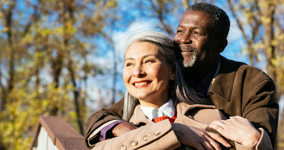 Older couple smile outdoors while embracing.