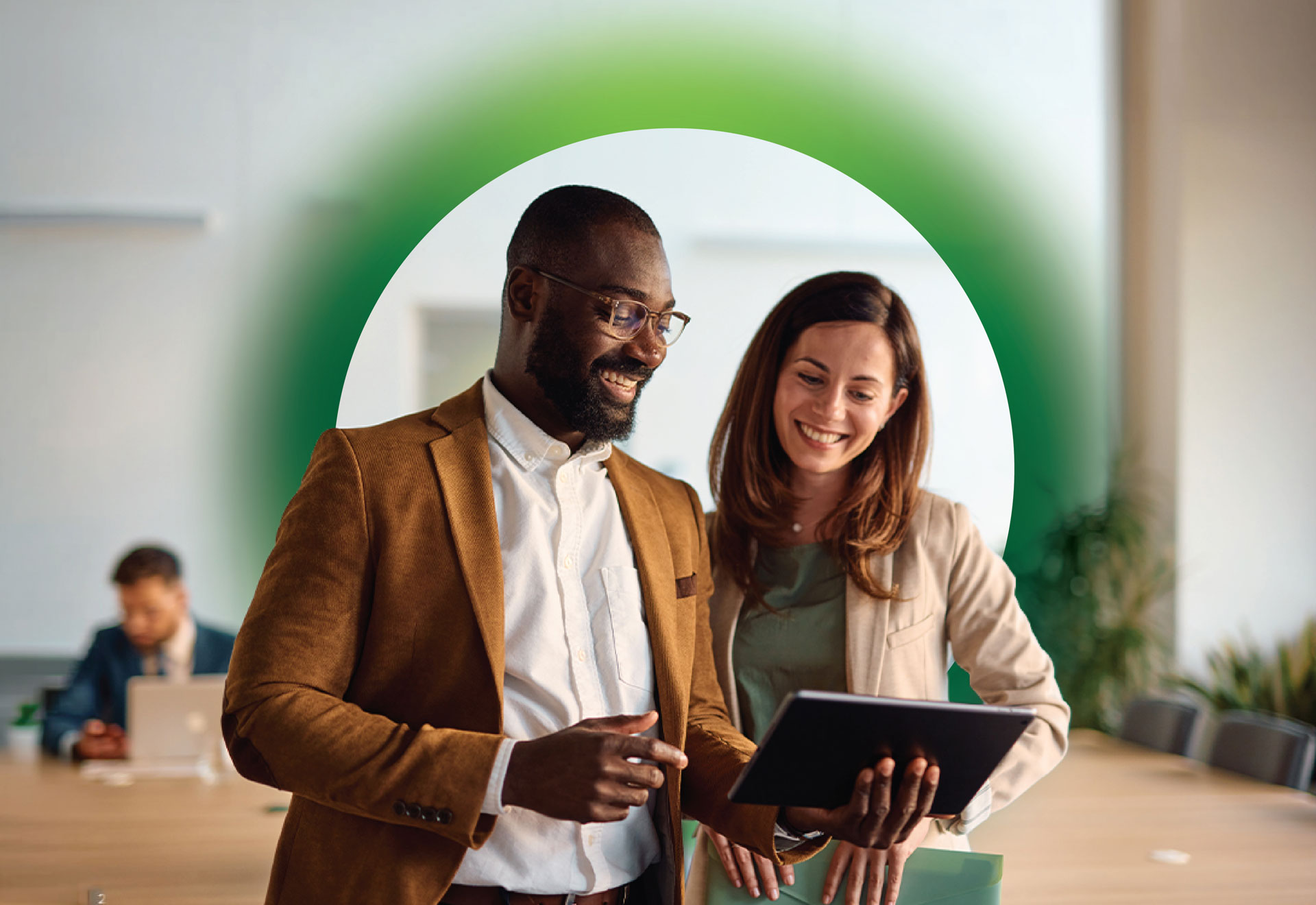 Two colleagues smile while looking at a tablet surrounded by a graphic green halo.