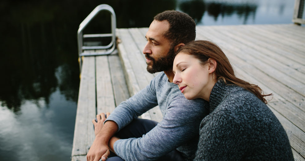 Couple sitting together on a dock by a lake.