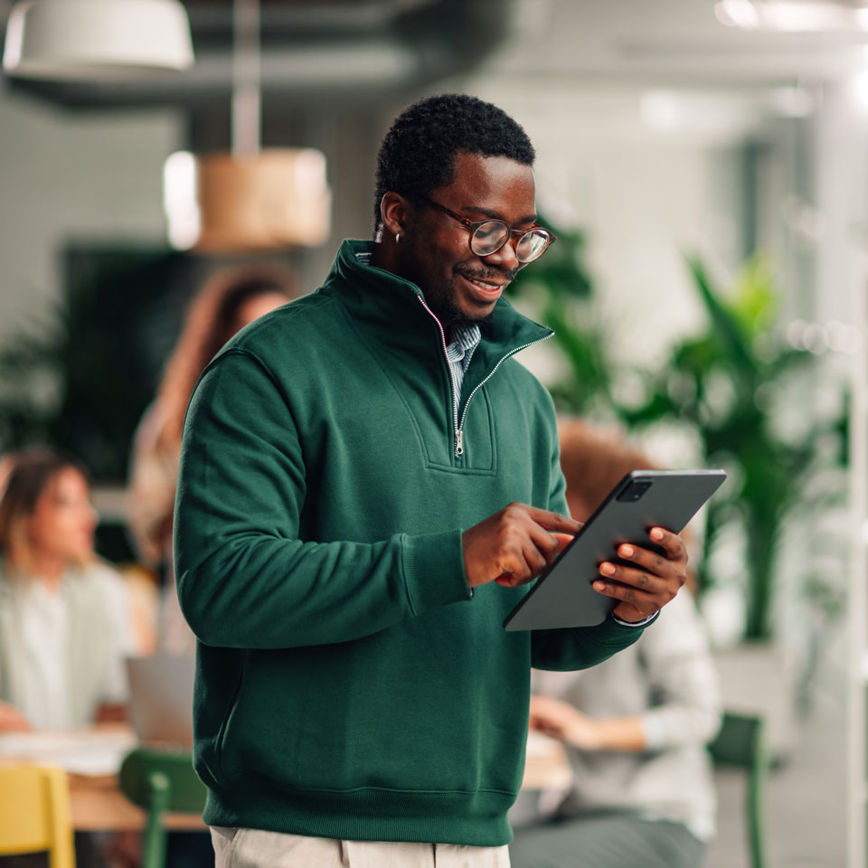 Person in a greens weater smiles while looking at a tablet.