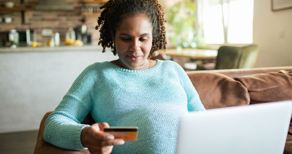 Person sits on a couch with an open laptop and a credit card in their hand.