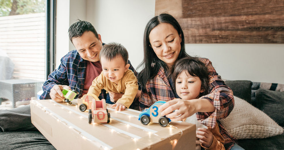 Family with young children plays cars together on a coffee table.
