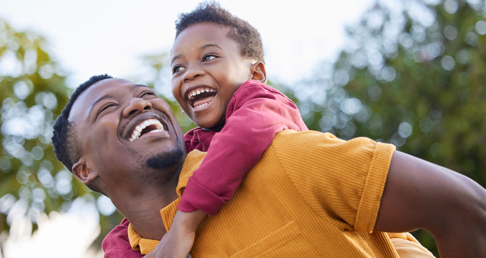 A child smiles while being carried on a parent's shoulders.