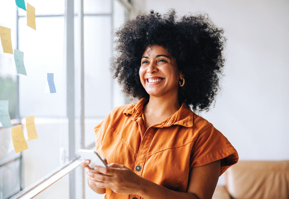 Person smiles while holding a smartphone in an office.