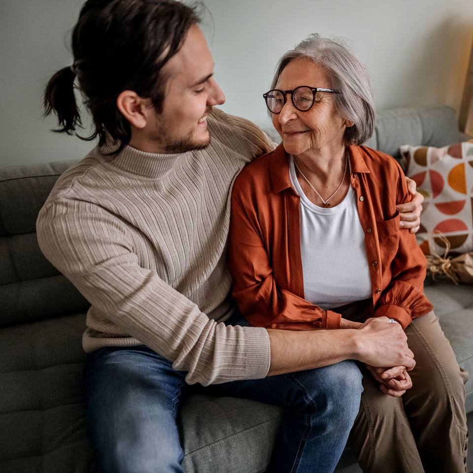 Person embraces an older family member while sitting on a couch.
