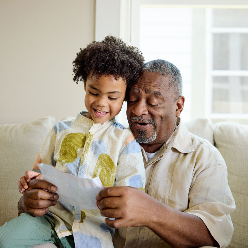 Young child sits on an older relative's lap and smiles while looking at a drawing.
